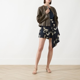Model wearing Max Mara Main Bouquet Cropped Leather Jacket in kaki, collarless with front buttons, styled with printed navy mini skirt and strappy
