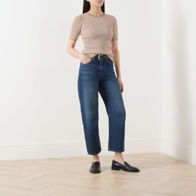 Model wearing dark blue cropped straight-leg jeans with a beige ribbed top and black loafers