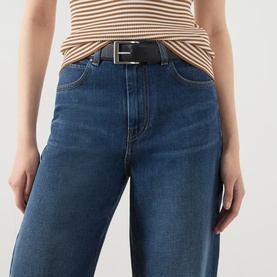 Model wearing wide-leg mid-blue jeans with black leather belt and striped tan and white top