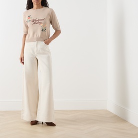 Model wearing Max Mara Weekend sand knit top with script embroidery, styled with wide-leg cream trousers and brown heeled boots.
