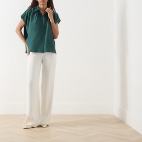 Model wearing Max Mara Weekend Crine Silk Shirt in dark green with collared neck and short sleeves, styled with white wide-leg trousers.