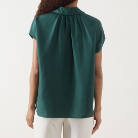 Model wearing Max Mara Weekend Crine Silk Shirt in dark green, showing pleated back detail and short sleeves, styled with white trousers
