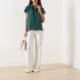 Model wearing Max Mara Weekend Crine Silk Shirt in dark green with white wide-leg trousers, carrying a small white bag.
