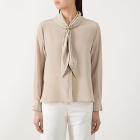 Model wearing Max Mara Main Dry Bow-Neck Silk Blouse in stone with long sleeves, tie-bow neck, and buttoned cuffs, styled with white trousers.