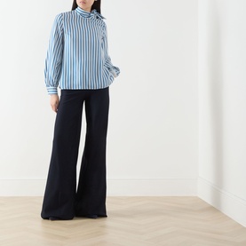 Model wearing Max Mara silk pinstripe shirt in blue and white with a bow neck, styled with wide-leg navy trousers.