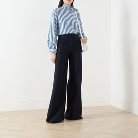 Model wearing Max Mara Main silk pinstripe shirt with navy wide-leg trousers and carrying a small white shoulder bag.
