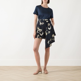 Model wearing navy floral print asymmetric mini skirt styled with a navy T-shirt and nude heeled mules