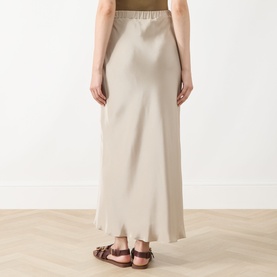 Model wearing Max Mara Main stone silk maxi skirt with elasticated waist, styled with brown sandals, seen from behind.