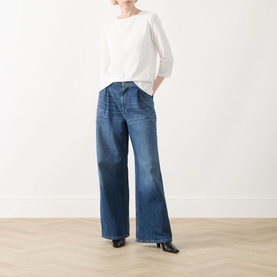 Model wearing Max Mara Weekend Multia Logo Top in white with round neck and three-quarter sleeves, styled with wide-leg blue jeans and black heels.