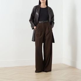 Model wearing Max Mara Weekend Multia Solid Black T-Shirt with wide-leg brown trousers, dark leather belt, and oversized leather coat.