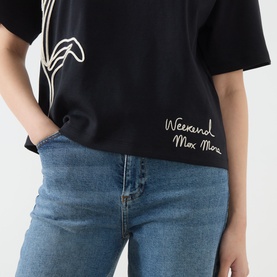 Model wearing Max Mara Weekend Sala Flower Boxy T-Shirt in black with embroidered flower motif and cursive logo, styled with blue jeans.