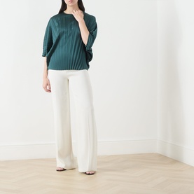 Model wearing Max Mara Weekend Aureo Pliss&eacute; Top in dark green with kimono sleeves, styled with wide-leg cream trousers and sandals.
