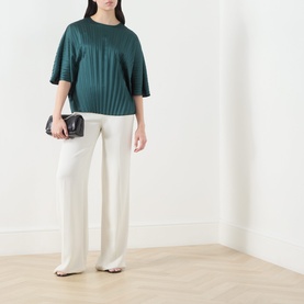 Model wearing Max Mara Weekend Aureo Pliss&eacute; Top in dark green with kimono sleeves, styled with white wide-leg trousers and small black bag.