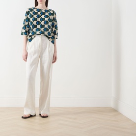 Model wearing Max Mara Weekend Adone Printed Blouse in dark green geometric print with cream wide-leg trousers and flat sandals