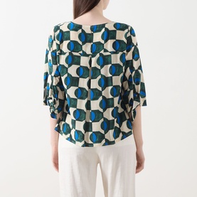 Model wearing Max Mara Weekend Adone Printed Blouse in dark green geometric print, back view, with white wide-leg trousers
