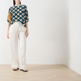 Model wearing Max Mara Weekend Adone Printed Blouse in dark green geometric print, styled with white wide-leg trousers and brown sandals.