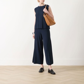 Model wearing Max Mara Weekend Ere Pliss&eacute; Top in navy, paired with wide-leg trousers, loafers, and a tan shoulder bag.
