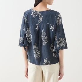Model wearing navy blue floral print linen top with short sleeves, styled with beige trousers, rear view
