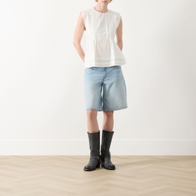 Model wearing Max Mara Weekend Vallo Peplum Blouse in white with sleeveless cap detail and peplum hem, styled with denim shorts and black boots