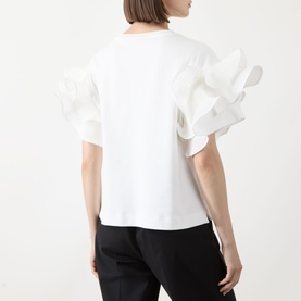 Model wearing Max Mara Main Costone Ruffle T-Shirt in white with oversized taffeta ruffle sleeves, styled with black trousers. Rear view.