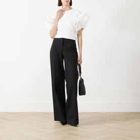 Model wearing Max Mara Main Costone Ruffle T-Shirt in white with ruffled taffeta sleeves, styled with black wide-leg trousers and black heels