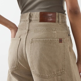 Model wearing Max Mara Weekend Arcadia Barrel-Leg Jeans in beige light denim, close-up of rear pockets with brown leather logo patch.