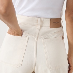 Model wearing Max Mara Weekend ecru cotton trousers, close-up of back pockets and leather logo patch, styled with white top.
