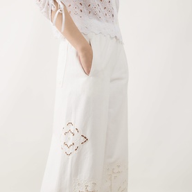 Model wearing Max Mara Weekend Guiliva Lace Cut-Out Wide-Leg Trousers in white with floral lace detailing, styled with a white broderie top.