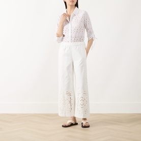 Model wearing Max Mara Weekend Guiliva Lace Cut-Out Wide-Leg Trousers in white with broderie detailing, styled with a white shirt and black sandals.