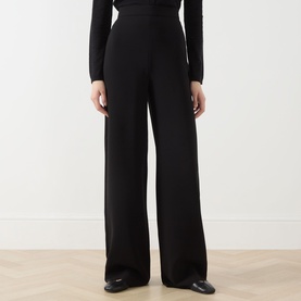 Model wearing black wide-leg high-waist trousers, styled with a black long-sleeve top and black leather shoes