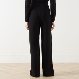 Model wearing black wide-leg trousers with high waist, styled with a black long-sleeve top, rear view