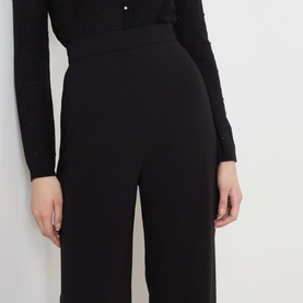 Model wearing black wide-leg trousers with wide waistband, styled with a black embellished knit cardigan