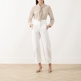 Model wearing Max Mara Main white cotton wide-leg trousers with high waist and turn-up hem, styled with beige tie-neck blouse and nude heels.