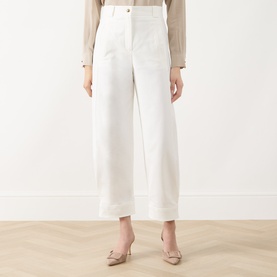 Model wearing Max Mara Main white wide-leg cotton trousers with turn-up hems, styled with a beige top and nude heels.
