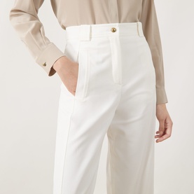 Model wearing Max Mara Main white wide-leg cotton trousers with gold-tone button detail, styled with a beige shirt.
