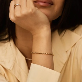 Model with Missoma gold beaded ball chain bracelet, styled with a matching gold ring and cream blazer