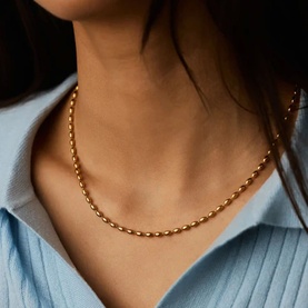 Model with Missoma gold oval-link chain necklace, styled with a light blue ribbed shirt