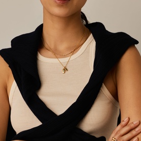 Model with Missoma gold chain necklace featuring a small pendant, layered styling visible, worn over cream ribbed top with black outerwear