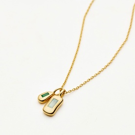 Missoma gold necklace with two rectangular pendant charms, one featuring a green stone and one with a pale blue-grey stone inset.