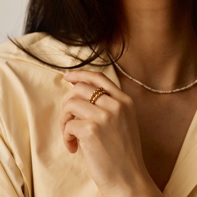 Model with Missoma gold stacked beaded rings, styled with a delicate gold chain necklace and cream satin shirt
