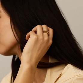 Model with Missoma gold stacked rings, worn together on index finger, featuring beaded and plain band styles