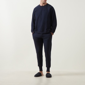Model wearing Paul Smith Access blue cotton joggers with matching navy sweatshirt and dark slip-on slippers.
