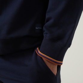 Model wearing Paul Smith Access blue cotton loungewear top, close-up of cuff with multicolour stripe trim and small logo embroidery.