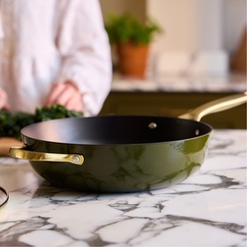 Stellar Cast Light Saut&eacute; Pan 28cm in olive with gold-tone handle, on marble surface, person preparing food in background.