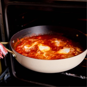 Stellar Cast Light Saut&eacute; Pan 28cm in clay with gold-tone handles, shown in oven with tomato and egg dish cooking inside.
