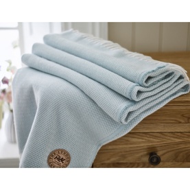 The Lyndon Company Arcadia Throw in blue, folded on a wooden surface, showing textured weave and branded circular patch detail.