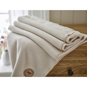 The Lyndon Company Arcadia Throw in Doeskin, folded to show textured knit weave and branded leather-look patch detail, on a wooden surface.