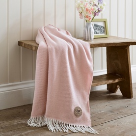 The Lyndon Company Arcadia Throw in rose, draped over a wooden bench with fringed edges and embroidered logo badge.