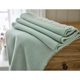 The Lyndon Company Arcadia Throw in sage green, folded and draped over a wooden surface with textured waffle-knit pattern visible.