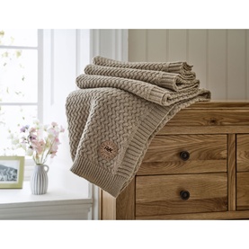 The Lyndon Company Cadenza Throw in Natural, cable-knit textured polyester, folded and draped over a wooden chest of drawers
